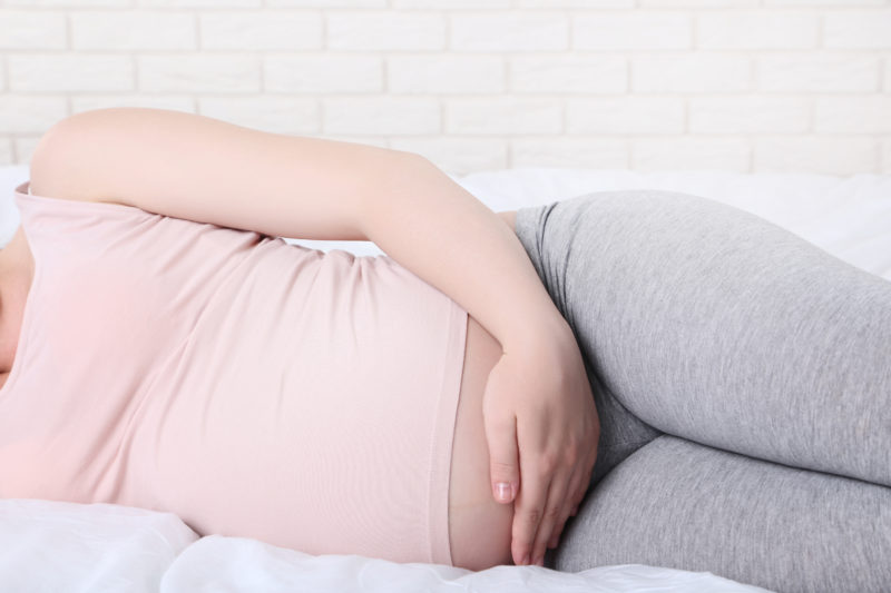 Pregnant Woman Lying on Side in Bed. Pelvic Pain in Pregnancy Affects 4%.